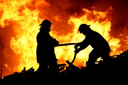 Silhouette of two firemen fighting a raging fire with huge flames of burning scrap timber